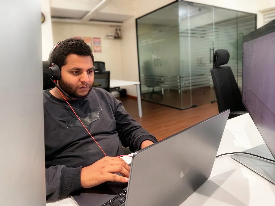An India Satcom developer pair-programming with headphones on a MacBook
